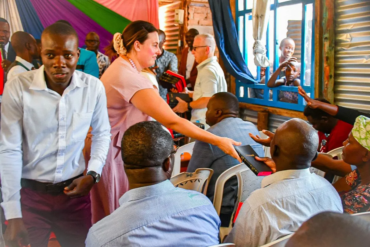 Claire handing a Bible to a seated man during a church visit in Kenya
