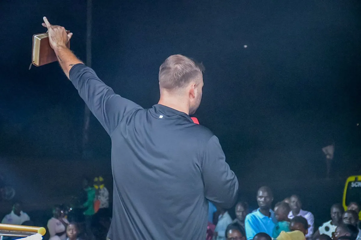 Trevor holding a Bible overhead before a crowd during an evening gathering in Kenya